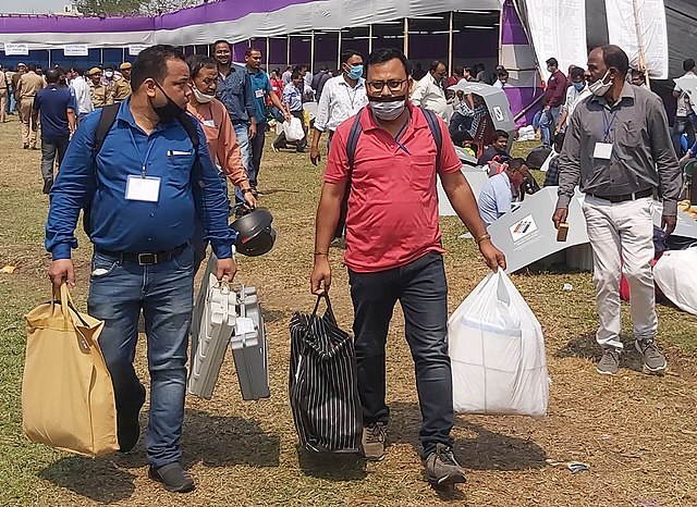 Polling officials carrying the Electronic Voting Machine (EVMs) and other necessary inputs required for the Assam Assembly Election, at a distribution
