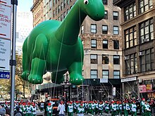 Many people carry along a balloon in the shape of a green dinosaur