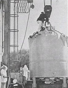 Large conical structure on a pulley with a man on top and two near the base.