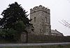 Square stone tower, behind a stone wall and partially obscured by a tree.