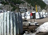 Large blocks of partially worked white marble lie on the ground at Colorado's Marble Mill site with the National Historical marker in the background.