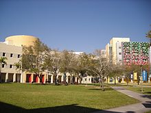 Several multistory buildings in the distance behind a plaza with trees