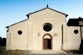 Fotografia colorida da fachada de uma igreja muito nua, com um alpendre encimado por um óculo