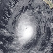 A photograph of a hurricane well to the southwest of the Baja California peninsula. The eye is small and oblong, and most of the thicker clouds are in the bottom-right quadrant of the hurricane.