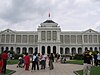 A building with columns painted white with a red flag mounted on the roof in the centre.