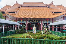 Photographie d'un temple bouddhiste traditionnel avec ses quatre pans de toit, son petit jardin à l'entrée, ses décorations et écritures chinoises.