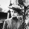 A young lady in a 1900s dress and a hat facing the viewer and looking to the right