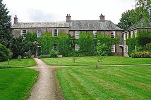 a group of two-storey buildings with Georgian-style multipane windows, seen across a lawn. The original farmhouse to the left has a central green-painted front door and windows to either side with three windows to the upper floor.