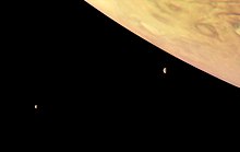 En haut à droite, on observe Jupiter orangée. Les deux lunes sont visibles devant le fond noir restant comme des croissants.