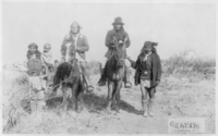 Geronimo, son, and two warriors. Originally captioned as "Geronimo's camp before surrender to General Crook, March 27, 1886: Geronimo and Natches mounted; Geronimo's son (Perico) standing at his side holding baby."