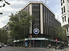 Fotografía de un edificio tomada desde la calle.  En la fachada de cristal, un logo redondo con las letras mayúsculas P y P sobre fondo azul.