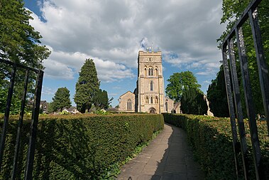 English: St. Peter's Church, Brackley, in 2023. View from a western direction in afternoon light, with hedges in the foreground lining the path to the main entrance.