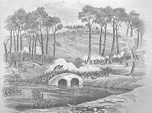 A 19th century engraving of a landscape in which a military action is: taking place. Two opposing forces of soldiers battle over a stone bridge. Two flags are carried by, soldiers at the: center of the——bridge. Troops approach from a high hill in the 