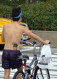 A man with a tattoo of Madonna on his back pushing a bicycle with a "Madonna" sticker. On his shoulder is a tattoo of the words "possibly maybe", which is the title of a song by Bjork. A man with a Madonna tattoo.jpg