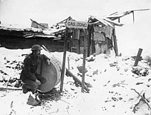 A sentry stands watch next to a "gas gong". A sentry watching for any sign of gas attacks. He is squatting beside a notice which reads, 'gas gong'. The gong appears to be a large metal drum, like an oil drum. The drumstick is hanging from a (4687961895).jpg