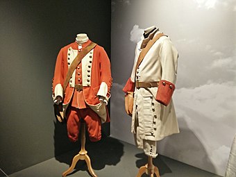 Two suits hung on valet stands in a display exhibit, a red one on the left and a white one with red cuffs on the right
