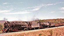 Un CFM] tren de vagones arrastrados por locomotoras de vapor cargados con mineral de hierro de la mina Ngwenya en el ferrocarril de Goba, Eswatini (entonces conocida como Swazilandia), 1970