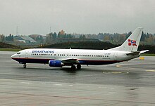 Ein mittelgroßer Passagierjet auf Asphalt mit weißem Oberteil und Heck und blauem Unterteil. Es gibt eine norwegische Flagge am Schwanz und 