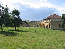 Pasto arborizado com construções antigas dispostas em L.