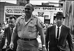 Sheriff Lawrence A. Rainey being escorted by two FBI agents to the federal courthouse in Meridian, Mississippi; October 1964 Lawrence Rainey flanked by FBI agents.jpg