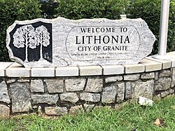 Stone sign with a depiction of two trees with the words Welcome to Lithonia City of Granite Donated by the Lithonia Summer Street Festival Committee May 18, 1996