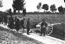 Photographie de militaires mettant en œuvre un canon de 75mm sur un chemin dans la campagne.