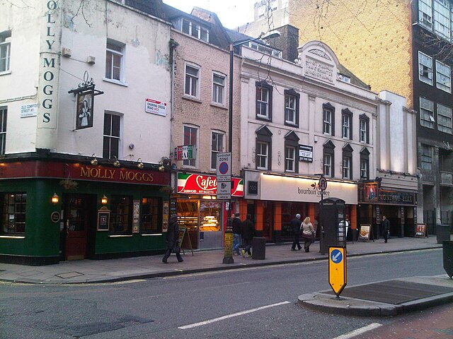 Charing Cross Road at the junction with Old Compton Street, with traffic island and grate through which a Little Compton Street sign is visible