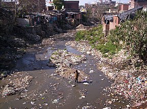 A child walks in a trash-laden river in the Indian Himalayas. Slum and dirty river.jpg