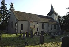 Fotografie einer Kirche mit verputzten Wänden und quadratischem Glockenturm.  Im Vordergrund sind mehrere Grabsteine ​​zu sehen