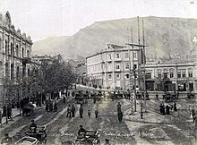 A picture of a city square with people walking about and people riding in carriages.