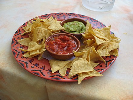 A bowl of tortilla chips with red salsa and green guacamole