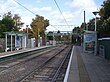 A set of two tram tracks between two platforms with shelters.