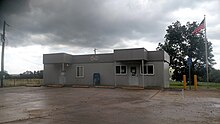 Fachada de la oficina de correos de Dennard. Edificio de una planta con bandera de Estados Unidos.