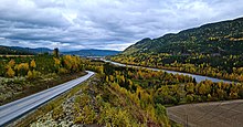 Foto einer Straße, die neben einem Fluss verläuft. In der Umgebung eine Herbstlandschaft.