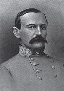 Un homme aux cheveux foncés et à la moustache pleine et sombre portant une veste militaire à col haut