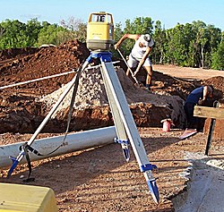 A rotary laser level set up and used to level sand fill in trenches. The graduated staff is leaning on the pile of sand. Laser-Level.jpg