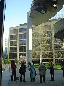 A full living room set hung inverted outside the MIT Media Lab in April 2010; it included an imitation stuffed cat curled in a chair, illustration of the MIT dome, and a floor lamp with the light left on. MIT hack living room set hung outside Media Lab.jpg
