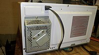 A white microwave oven is shown sitting on a workbench, showing fan guarding and cover screws