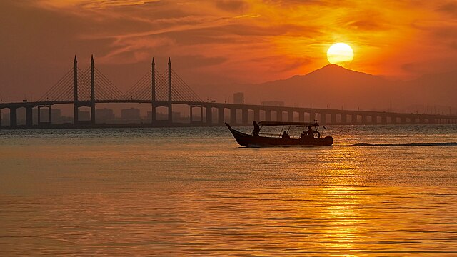 Guide to Penang Island on a boat passing the sea bridge at sunrise.