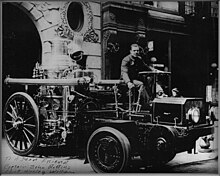 Firefighter Wesley Williams; Engineer of Steamer operating Christie Tractor at 363 Broome St; Engine 55 in Little Italy NYC; circa 1920. The tractor had 2 wheels and pulled the steam fire engine (rear end with large wheels) in place of the Percheron draft horses. Wesley Williams EngineerOfSteamer ChristieTractor BroomeSt.jpg