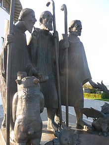 estatua de tres monjes caminando con sus palos, escoltados por animales fantásticos