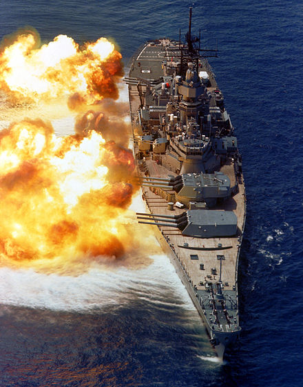 The firepower of a battleship demonstrated by USS Iowa (c. 1984). The muzzle blasts are large enough to distort the ocean surface.