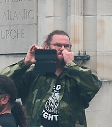 A white man holding up a smartphone and biting his fingernails