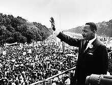 Martin Luther King Jr. waves to a large crowd while standing in the National Mall.