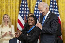 Un homme en costume remet à une femme souriante une médaille.