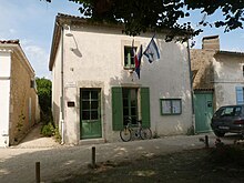 Fotografia del municipio di Talmont, un piccolo edificio in stile Saintonge riparato da un tiglio e circondato da malvarosa