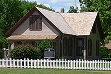 Maison à un étage et demi avec toit à deux versants et petit porche avant ;  entouré de palissade