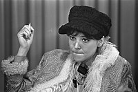 Young seated woman in a black cap, holding a cigarette