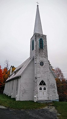 Dřevěný kostel natřený na bílo s věží převyšovanou věží.