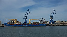 Foto eines blauen Containerschiffs, angedockt in einem Hafen.